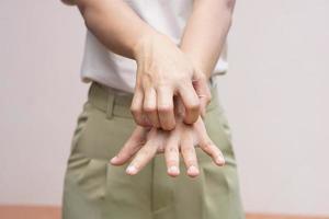 mujer rascándose el brazo por picazón en un fondo gris claro. la causa de la picazón en la piel incluye el concepto de picaduras de insectos de la piel para el cuidado de la salud. foto