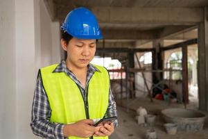 Asian engineer, Young Architect or contractor put on a helmet for safety and use smart phone for take picture and send construction defect to head office. Construction Site and contractor photo