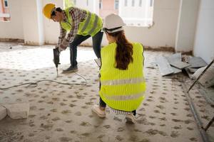 Engineer checking worker using an electric jackhammer to drill perforator equipment making holes before pouring the floor to be strong at construction site, Concept of worker and residential building photo