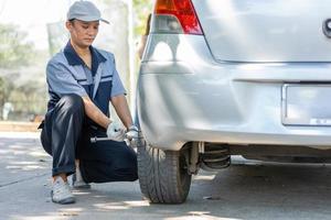 Expertise mechanic man  in uniform using force trying to unscrew the wheel bolts nuts and help a woman for changing car wheel on the highway, car service, repair, maintenance concept. photo
