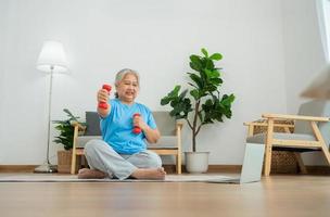 anciana asiática levantando pesas para hacer ejercicio y hacer ejercicio en casa. mujer madura activa haciendo ejercicio de estiramiento en la sala de estar. ejercicio activo y saludable para personas mayores, mayores y mayores.