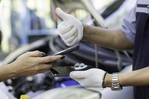 Asian women get contact numbers from Asian male auto mechanics after fixing the car engine problem and QR code scan to pay for fixing vehicle service. Car repair, and maintenance concept. photo