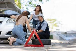 Expertise mechanic man  in uniform using force trying to unscrew the wheel bolts nuts and help a woman for changing car wheel on the highway, car service, repair, maintenance concept. photo