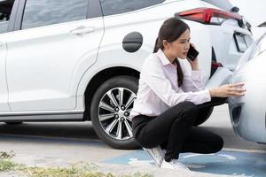 la conductora asiática verifica los daños después de un accidente automovilístico antes de tomar fotografías y enviar un seguro. reclamo de seguro de accidente automovilístico en línea después de enviar fotos y evidencia a una compañía de seguros.