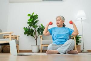 anciana asiática levantando pesas para hacer ejercicio y hacer ejercicio en casa. mujer madura activa haciendo ejercicio de estiramiento en la sala de estar. ejercicio activo y saludable para personas mayores, mayores y mayores.