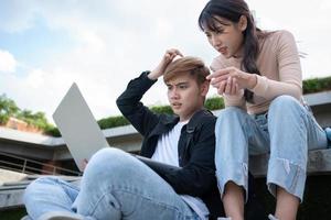 Asian students sitting on step are excited and stressed and disappointed after check exam results in computer laptops, Entrepreneurs disappointed after Project fall. Student lifestyle in university photo