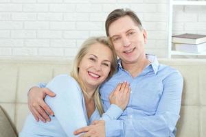 Middle aged couple relaxing on the couch smiling at camera at home in the living room photo