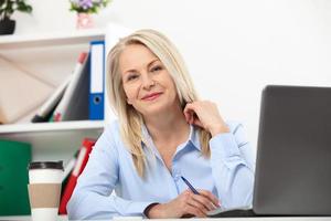 Her job is her life. Business woman working in office with documents. Beautiful middle aged woman looking at camera with smile while siting in the office. photo