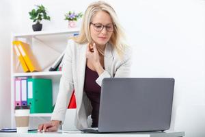Working on new project. Business woman with glasses working in office with documents. Beautiful middle aged woman looking at laptop with smile while siting in the office. photo