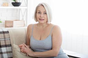 Active beautiful middle-aged woman smiling friendly and looking in camera in living room. Woman's face close up. Realistic images without retouching with their own imperfections. Selective focus. photo