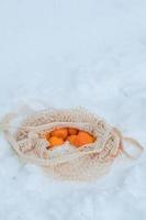 tangerines in an open string bag lie on the snow. Picnic in winter in winter forest photo