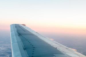 pink sunset from above, over winter terrain and airplane wing photo
