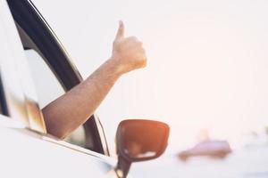 Portrait of happy smiling Young asian man traveler on the road showing thumbs up while driving in his car. photo