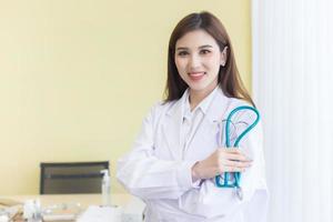 Young beautiful  Asian woman doctor Standing with arms crossed happy and smile in hospital. Wearing a white robe and stethoscope photo