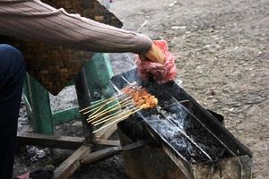 Photo of a satay being grilled on a grill in a market area in Bali.