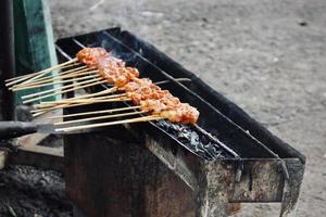 Photo of a satay being grilled on a grill in a market area in Bali.