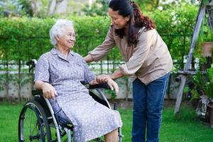 cuidador ayuda a una anciana asiática con discapacidad a una paciente sentada en silla de ruedas en el parque, concepto médico. foto