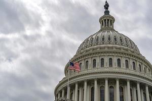 Washington DC Capitol with waving flag on sky background photo