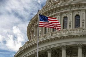 Washington DC Capitol with waving flag on sky background photo