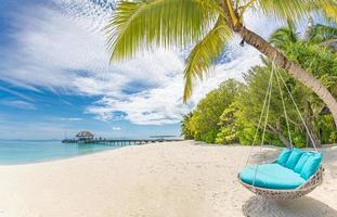 Tropical beach panorama as summer landscape with beach swing or hammock and white sand and calm sea for beach banner. Perfect beach scene vacation and summer holiday concept. Boost up color process photo