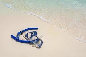 Summer beach coastline snorkel gear, googles on soft sand calm waves splashing. Tropical summer shore closeup, freedom adventure, outdoor recreation. Relaxing view of recreational activity, snorkeling photo