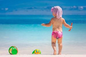 Toddler cute baby girl is playing on a beach near a sea. Adorable toddler girl playing with beach toys on white sand beach, luxury family vacation, exotic beach view photo