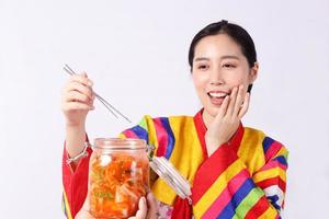 hermosa mujer coreana con hanbok sosteniendo palillos recoge kimchi en un frasco de vidrio los ingredientes incluyen repollo blanco, zanahoria, rábano, jengibre, manzana, chile y sal. concepto de comida fermentada, coreano foto