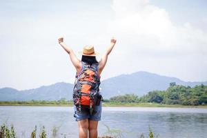 una mujer asiática que lleva una mochila de senderismo. ella levanta los brazos. siéntete divertido y feliz. concepto de negocio de turismo de naturaleza foto