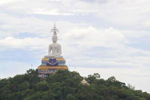 white Buddha image on a high mountain, built with the belief of Buddhism as a spiritual anchor and surrounded by green trees, sharpens the high mountains. photo