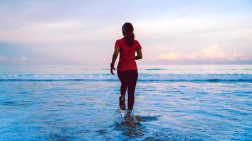 chica corriendo entrenamiento trotar en la playa por la mañana. relájate y feliz corriendo en el mar. en verano foto
