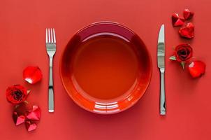 concepto de comedor de san valentín con plato rojo, tenedor y cuchillo colocados en una mesa roja con papel de rosa y forma de amor. foto