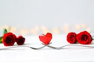 Red heart shape paper fold put on two forks with roses put on white table and bokeh light background for Valentines concept. photo