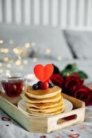 Valentine's day breakfast or brunch. Homemade pancakes with berries, cup of tea and red roses. Copy space photo