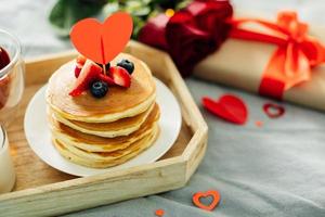 Valentine's day breakfast concept. Pancakes with berries, roses flowers, cup of tea, gift box. photo