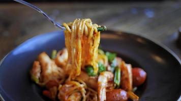 Close up, selective focus, Italian pasta spaghetti with prawns in Tom Yum flavor, Thai style pasta, tasty and spicy, delicious menu in dark color plate on wooden table photo