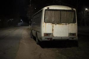 White bus is on side of road at night. Illegal parking along road. photo