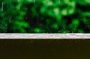 toma cinematográfica de gotas de lluvia que caen del cielo gris y sobre la superficie húmeda de la baranda de un balcón, creando ondas en el agua quieta foto