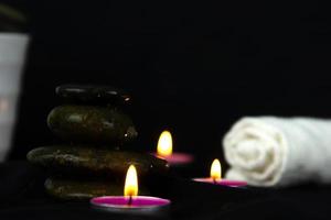 Layers of stones are on dark background, two rounded candles with white towel, use for massage and yoga obect concepts. photo