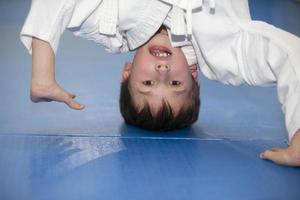 A small boy in a kimano upside down. The child is engaged in judo or karate. Section for children of combat sports. photo