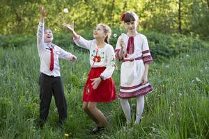 niños ucranianos o bielorrusos con camisas bordadas juegan en el prado. foto