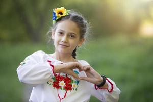 A little Ukrainian and Belarusian girl in an embroidered shirt shows a heart sign with her fingers. photo