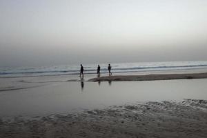 lonely beach with people strolling on the sand at the edge of the sea waves photo