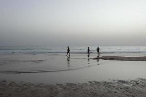 lonely beach with people strolling on the sand at the edge of the sea waves photo