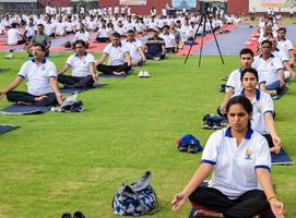 New Delhi, India, June 21 2022 - Group Yoga exercise session for people at Yamuna Sports Complex in Delhi on International Yoga Day, Big group of adults attending yoga class in cricket stadium photo