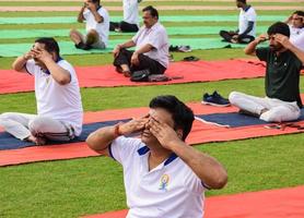 nueva delhi, india, 21 de junio de 2022 - sesión grupal de ejercicios de yoga para personas en el complejo deportivo yamuna en delhi el día internacional del yoga, gran grupo de adultos que asisten a clases de yoga en el estadio de cricket foto