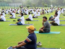 New Delhi, India, June 21 2022 - Group Yoga exercise session for people at Yamuna Sports Complex in Delhi on International Yoga Day, Big group of adults attending yoga class in cricket stadium photo