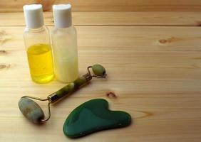 Jade roller and gouache scraper, bottles with cosmetics on a wooden table. photo
