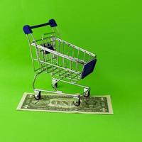 A shopping cart stands on a 1 dollar bill on a green background. photo