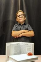 a boy with glasses folded his arms on his chest, a serious look, a stack of books, back to school