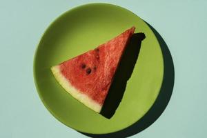 watermelon slice on a green plate on a turquoise background, top view photo